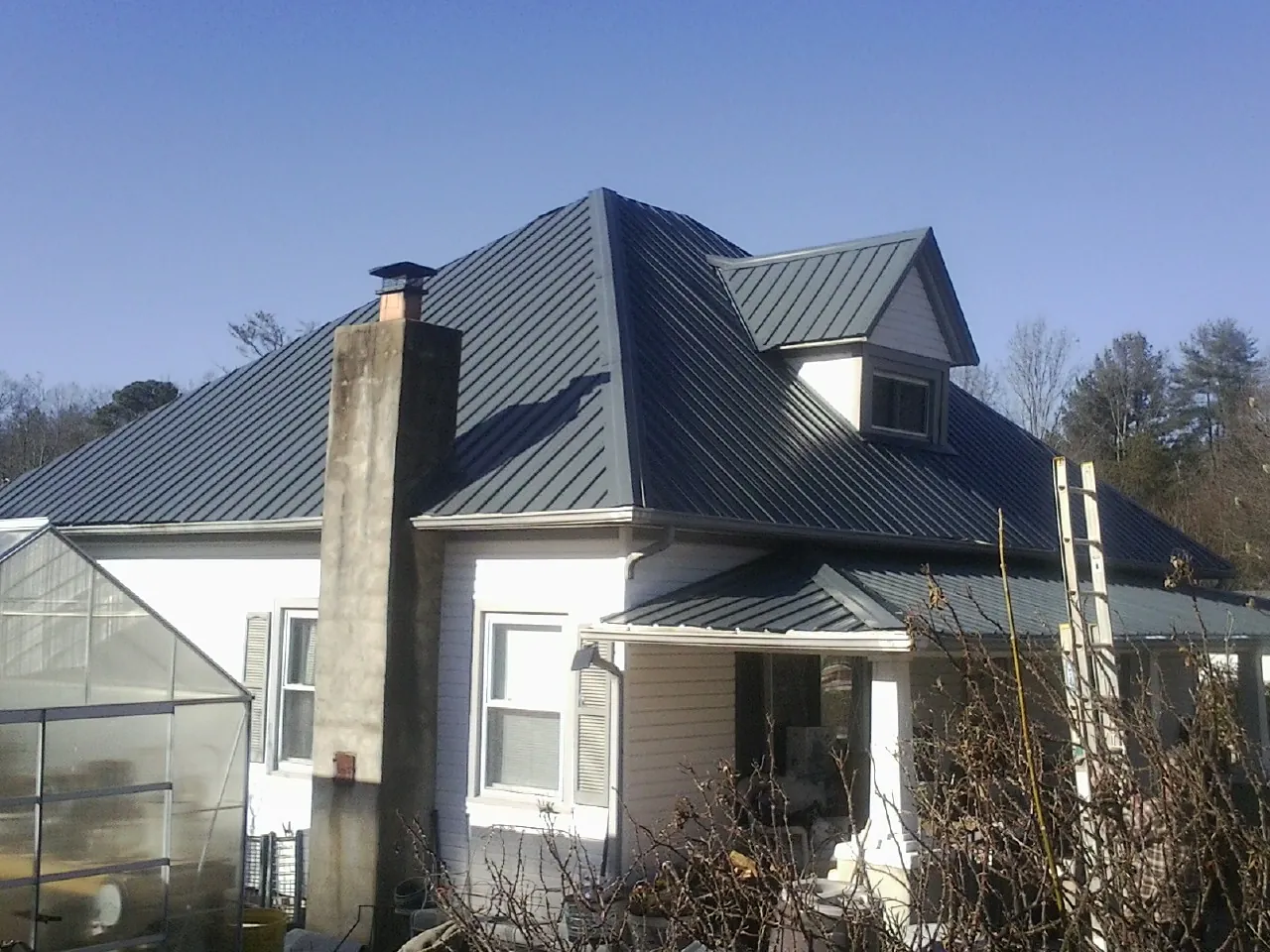 Dark blue standing seam metal roof on a white farmhouse with dormer — Slate & Tile Roof Repair by Roofing Brothers in Berkeley Heights