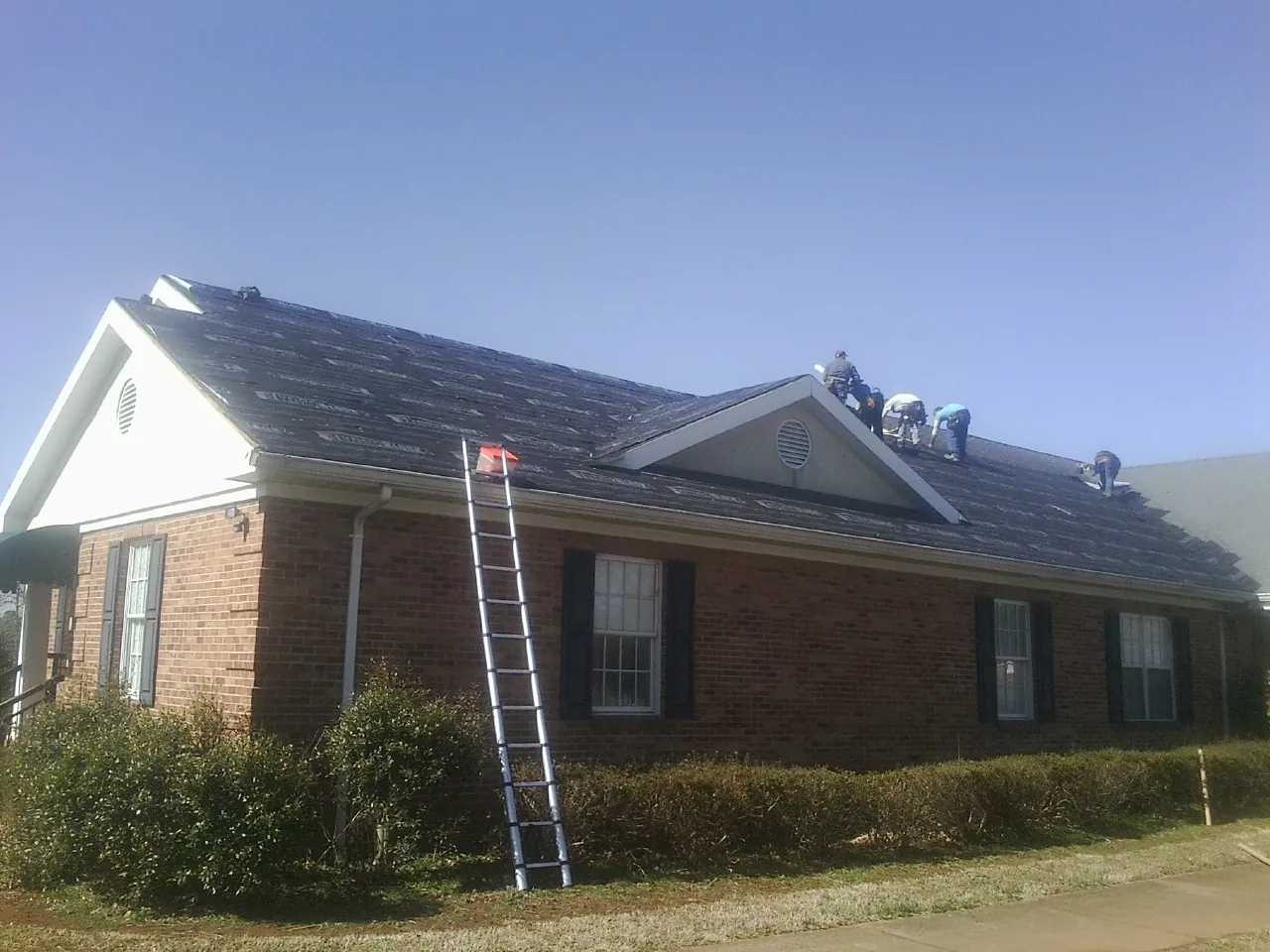 Crew tearing shingles off a brick ranch roof with a ladder set — Emergency Roof Repair work by our crew in Berkeley Heights