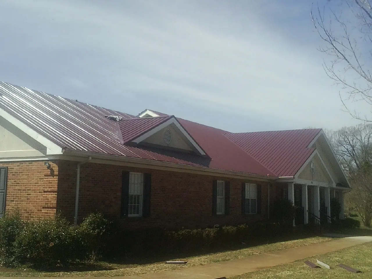 Red metal roof with gabled entries on a long brick building, from a Hail Damage Roof Repair job in Berkeley Heights