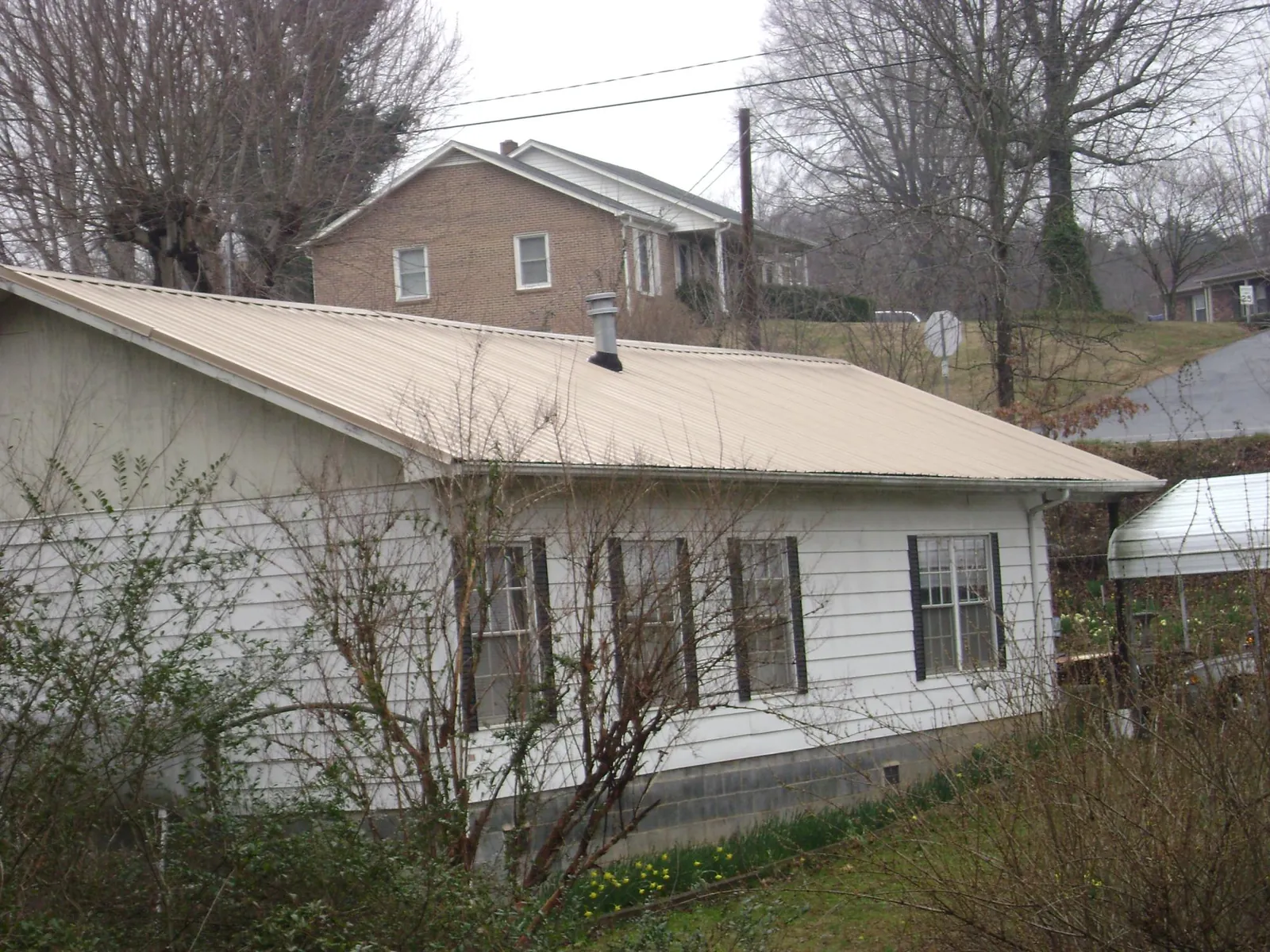 Tan metal roof on a white sided house set into a hillside — Commercial Roofing by Roofing Brothers in Berkeley Heights